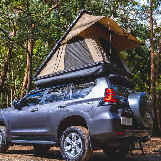 SUV with a rooftop tent setup in a wooded camping area.