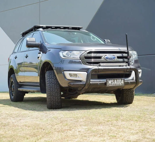 SUV with a bull bar and roof rack, parked on grass near a modern building.
