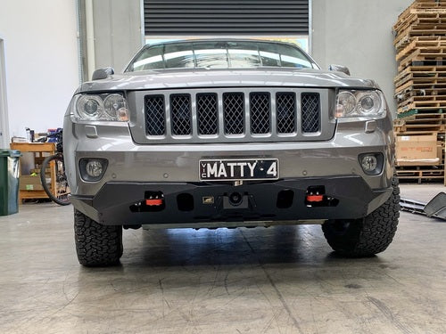 Front view of black Jeep with reinforced bumper, red tow hooks, outdoors.