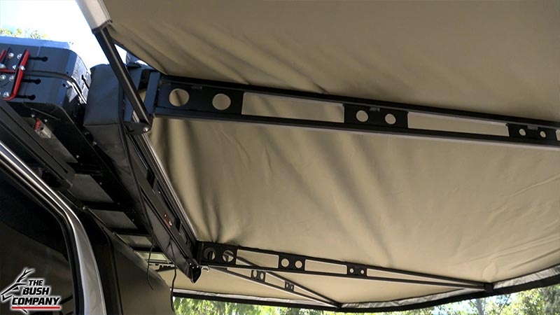 White pickup truck under tan rooftop tent and awning, trees and sky visible.