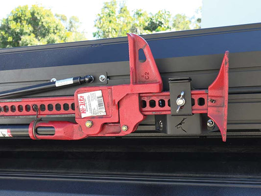 Red high-lift jack mounted on black frame, secured with attachment, trees behind. 800