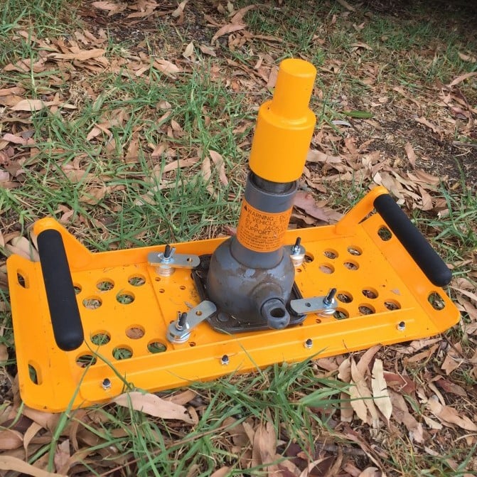 Yellow mechanical device with handles, on grass and fallen leaves.