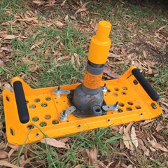 Yellow mechanical device with handles, on grass and fallen leaves.