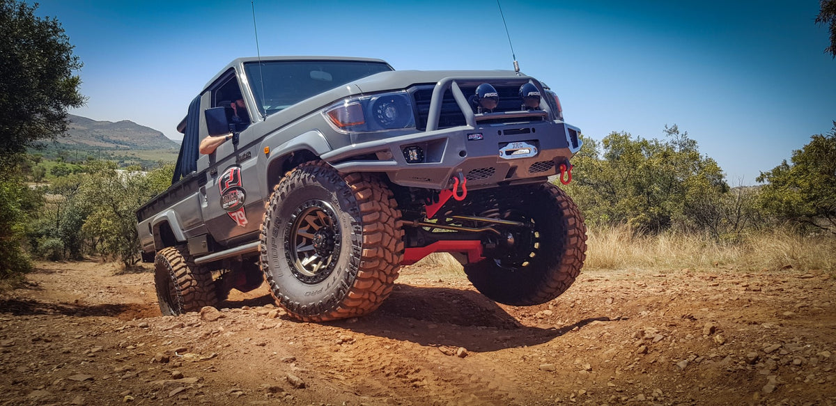 Off-road truck on rocky terrain, large tires, rugged build, equipped front bumper with winch.