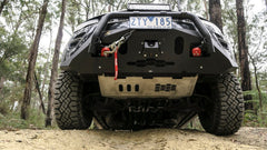 View beneath raised 4x4 in forest, showing license plate, bumper, and winch.