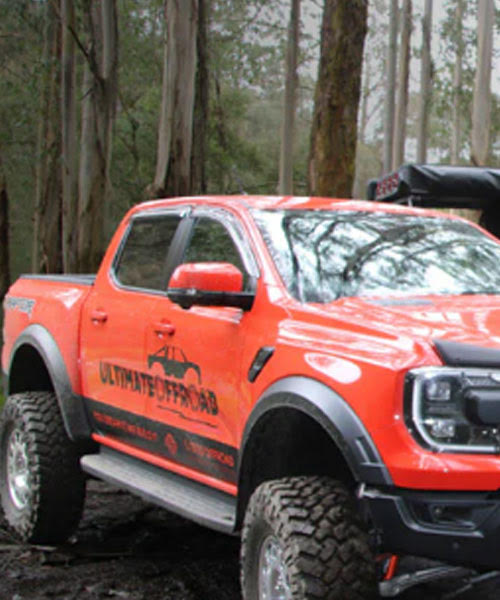 Ultimate Offroad logo on orange truck in forest.