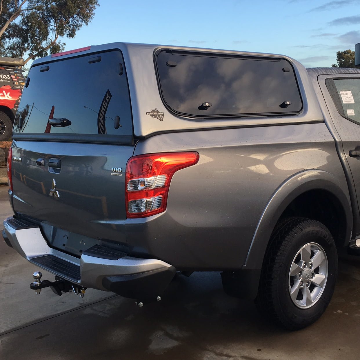 Silver Mitsubishi pickup with closed canopy parked on wet surface.